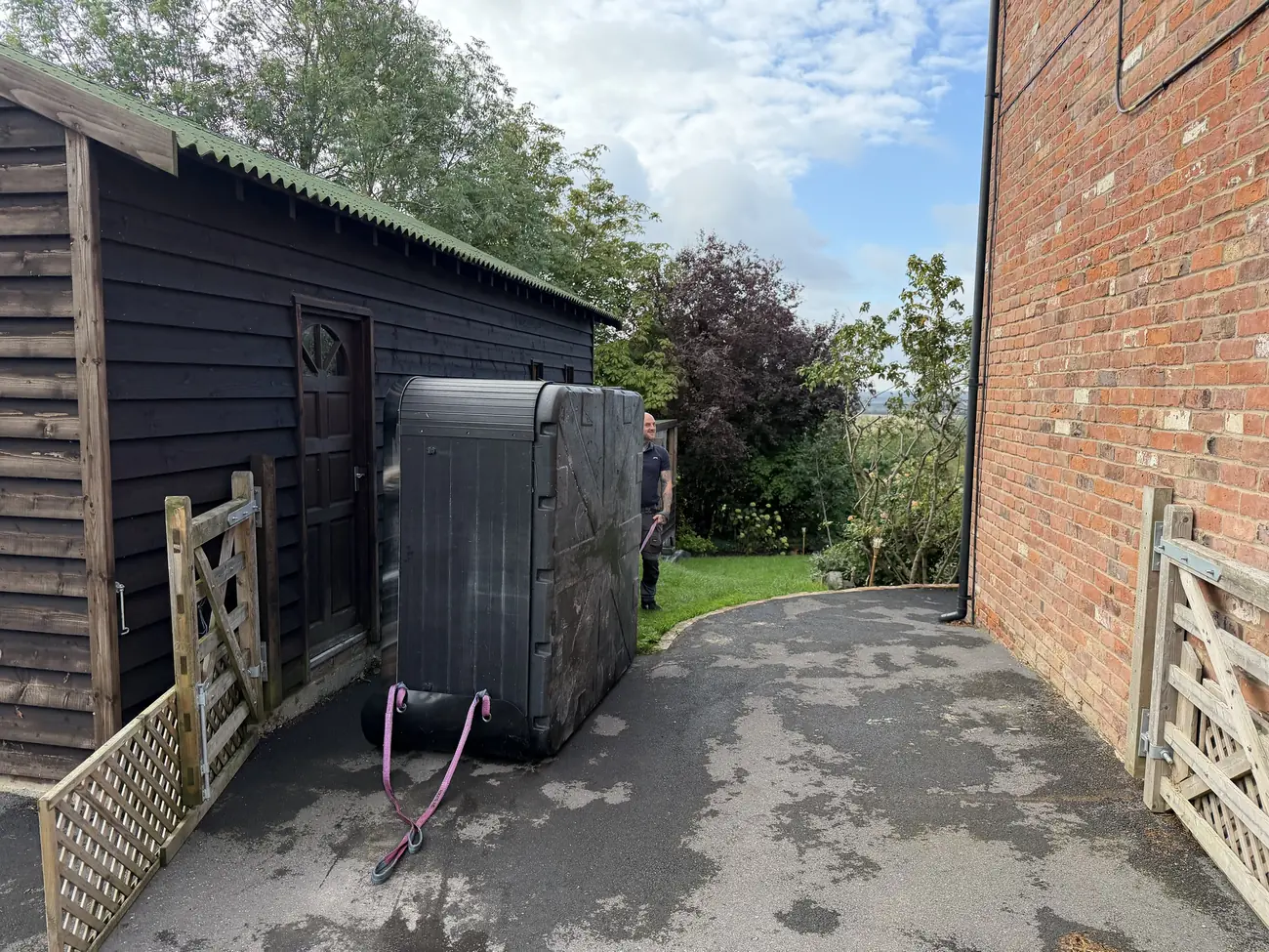 Hot tub stood on end being moved past a garden gate by a TopTubs engineer