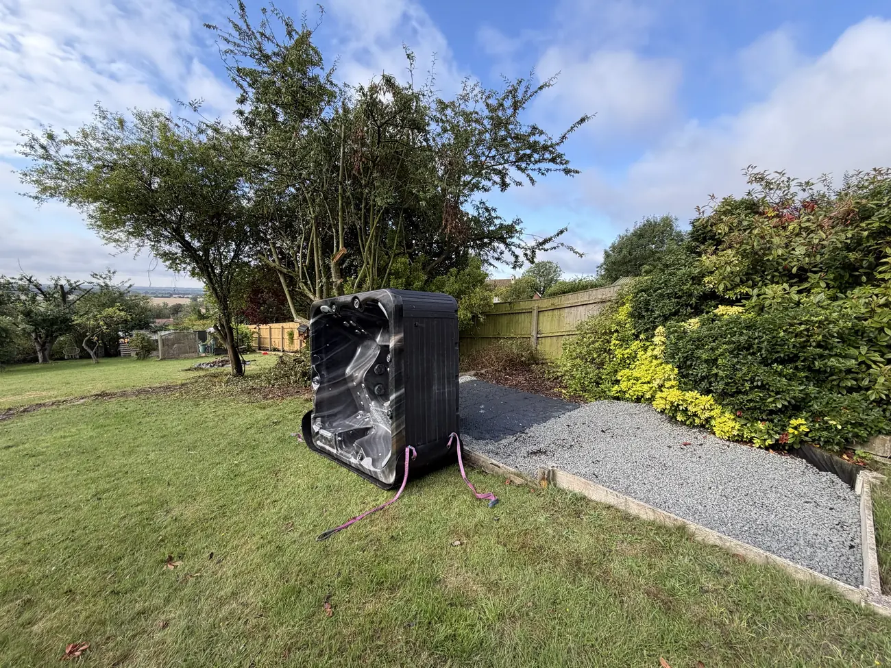 Hot tub stood on end on a skid board being moved across a lawn
